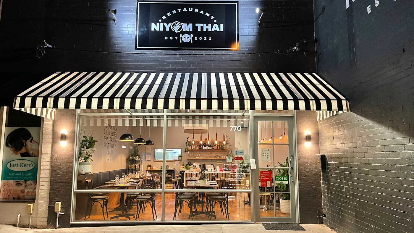The Niyom Thai storefront at night with its black-and-white striped awning.